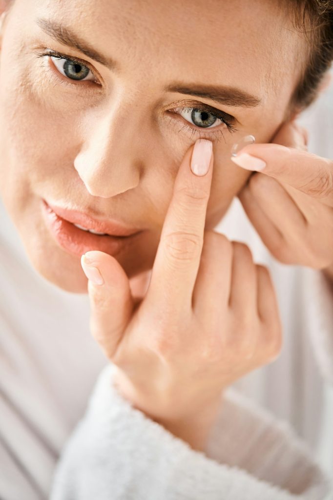 beautiful woman in white comfy bathrobe wearing her contact lenses near mirror in bathroom