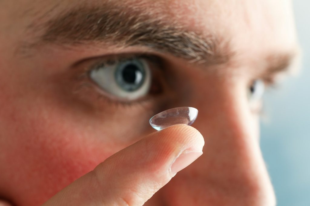 Inserting a corrective contact lens. Man with blue eyes